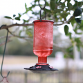A red bird water feeder hanging on a tree. 