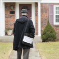 A census worker wearing a black hat and coat walking up to a house.