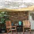 Two wooden chairs on a porch underneath a tan shade sail. 
