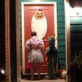 Two children waiting at a well-lit door for Halloween treats.