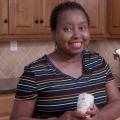 A woman stands in a kitchen while holding a can of reduced fat cream of chicken soup. 