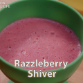 A pink blended raspberry dessert in a green cup.