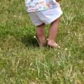 A small child runs barefoot through tall grass and has red insect bites on his calf. 