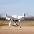 A close up shows a drone hovering above an open field. 