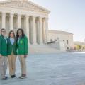Three female teenagers wearing green blazers and khaki pants standing in front of the Supreme Court Building in Washington, D.C.