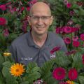 A smiling man with a polo listing his name as “Dr. Eddie Smith” is surrounded by colorful flowers.