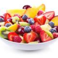 A white bowl of mixed chopped fresh fruits and berries on white background.