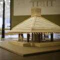 A wooden model of a building rests on a table in an exhibit hall.
