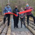 Four people stand on a bridge while cutting a ceremonial ribbon.