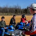 Three young people sit on ATVs as they listen to their instructor.