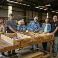 A group of people stand in a shop around a woodwork project.