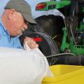 A man pours a bag into a yellow hopper on a tractor.