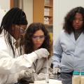 Three girls in lab coats work with scientific equipment.