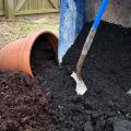 A shovel stands among soil from a wheelbarrow and a pot.