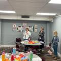 A group in a circle holds a white string that crisscrosses a classroom.