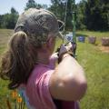 A young person pulls back a bow while aiming at a target.