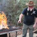 A man points at hot metal he just heated in a fire to forge it.