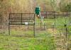 Two sturdy wire gates are raised in the large round corral trap. An automatic feeder on a tall tripod is inside the pen.