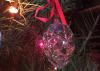 A small pink stocking with a white fuzzy top hangs from a Christmas tree inside a house.