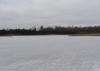 Ice covers a large pond with trees on the far side.