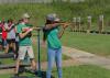 Teenagers at a shooting sports competition aim shotguns at targets.