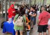 Several adults and children gather around an educational booth hosted by a man in a crawfish suit.