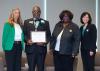 Four people stand in a line for a plaque presentation.