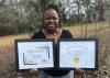 A woman holds two framed certificates.