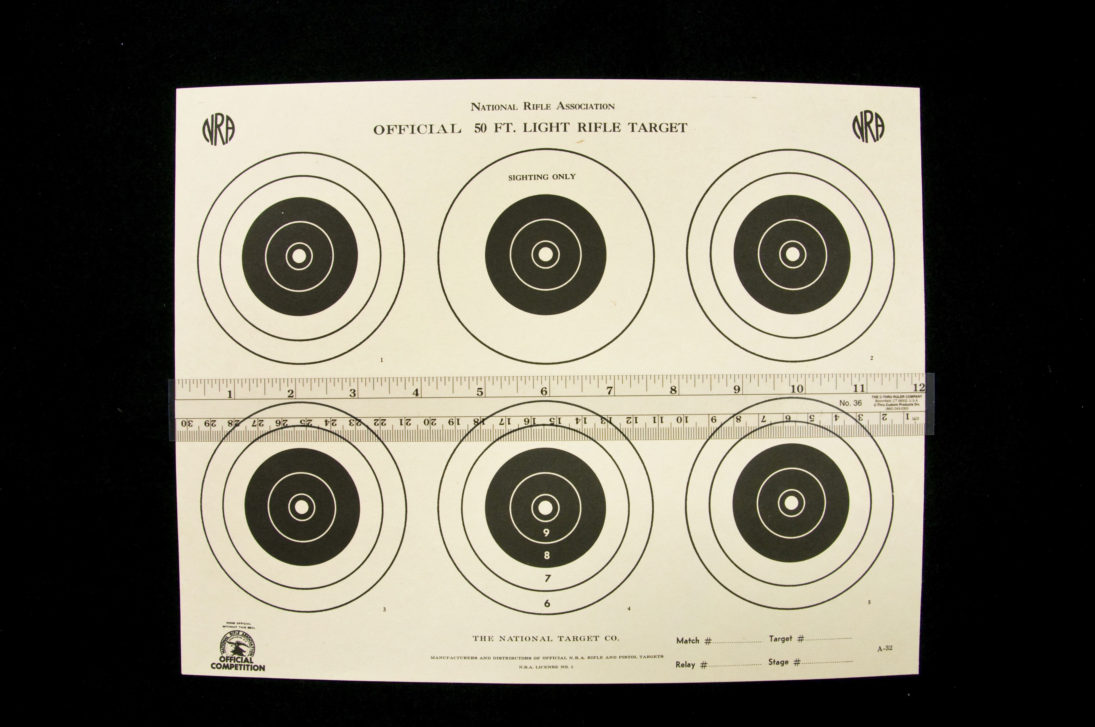 National Rifle Association 50 Ft. Rifle Target with six targets all of which have two larger white outer circles and three smaller inner black circles with a little white dot in the middle except for one on the top middle has one large white outer circle with three smaller inner black circles with a little white dot in the middle labeled SIGHTING ONLY, and the target has a ruler lying horizontally in the middle of the sheet.