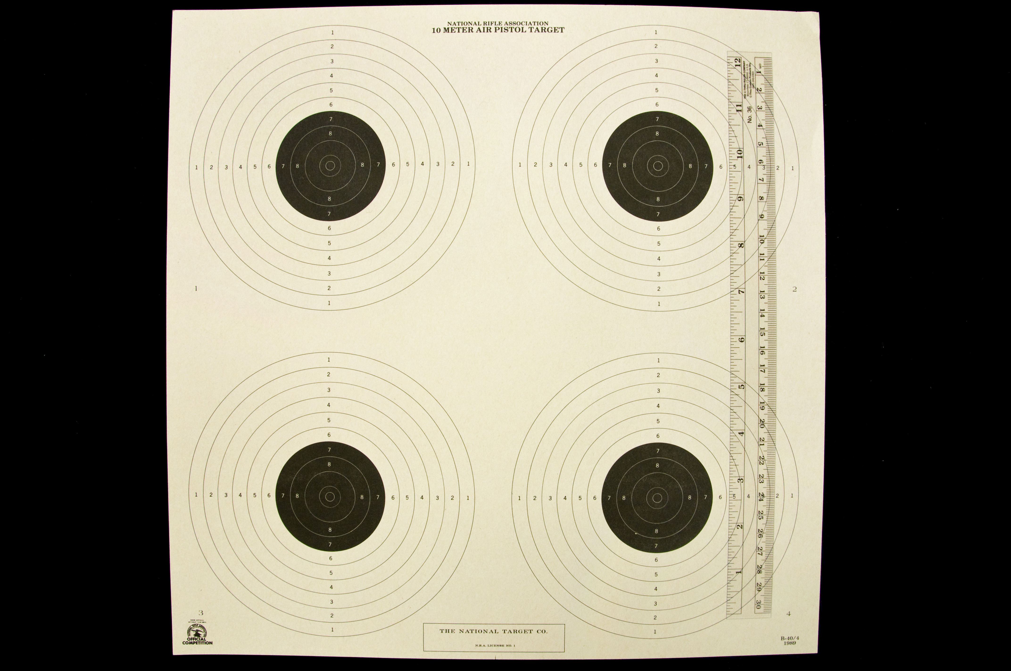 National Rifle Association 10 Meter Air Pistol Target with four targets with six white outer circles and five smaller inner black circles with a ruler lying vertically on the right of the target.