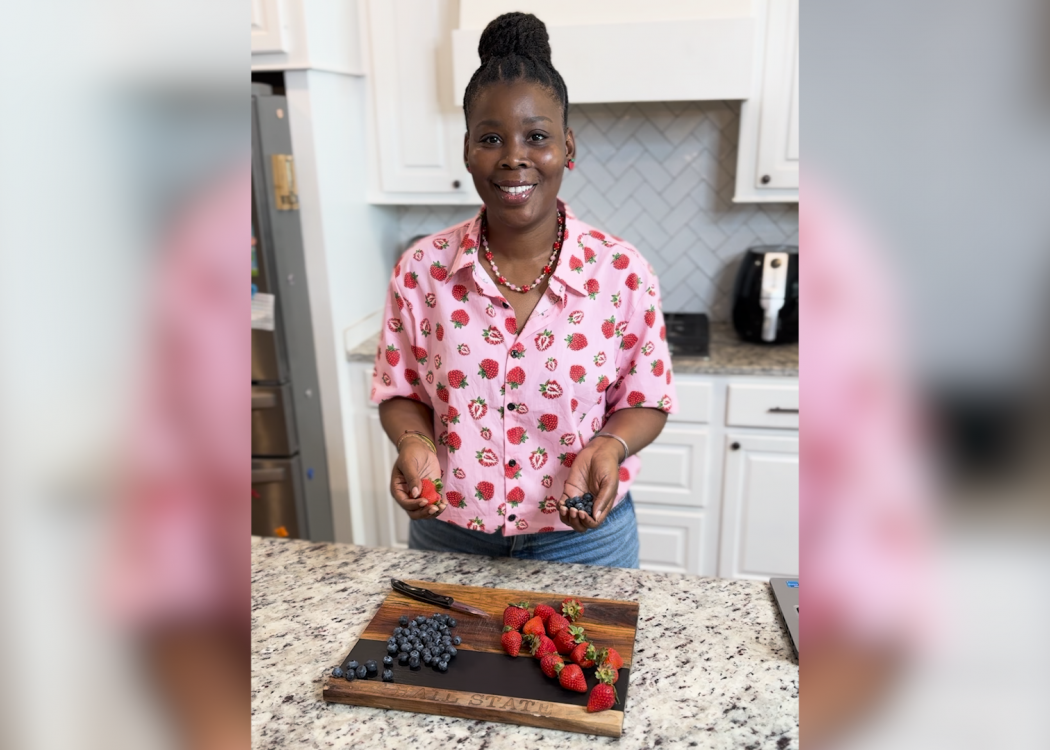 A woman stands in a kitchen with strawberries on a cutting board.