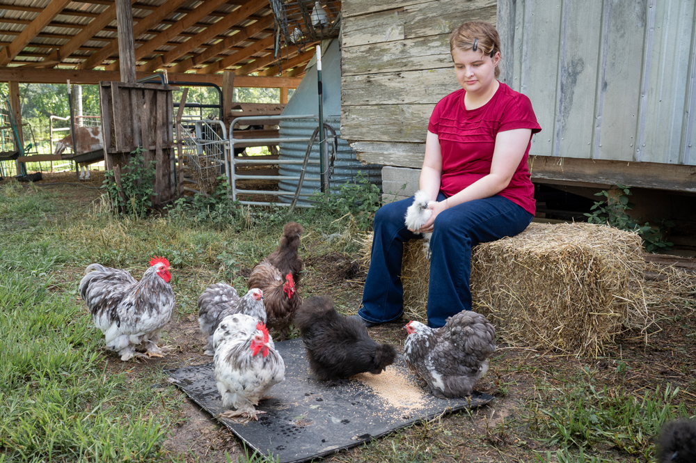 A child surrounded by chickens and holding a chick.