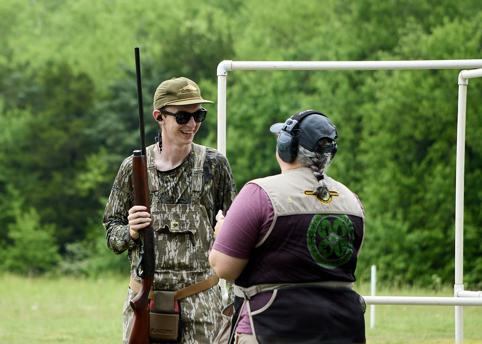 A teen holds a gun vertically while an adult watches.