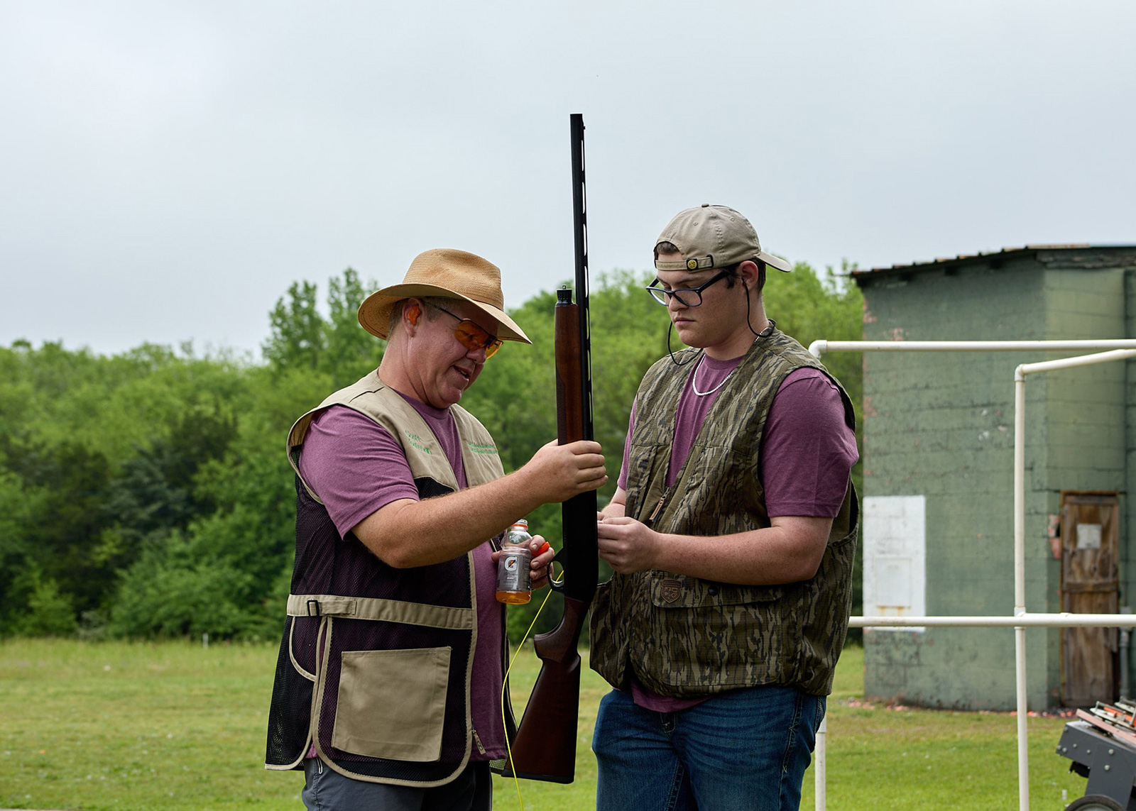 An adult holds a gun vertically while a teen watches.