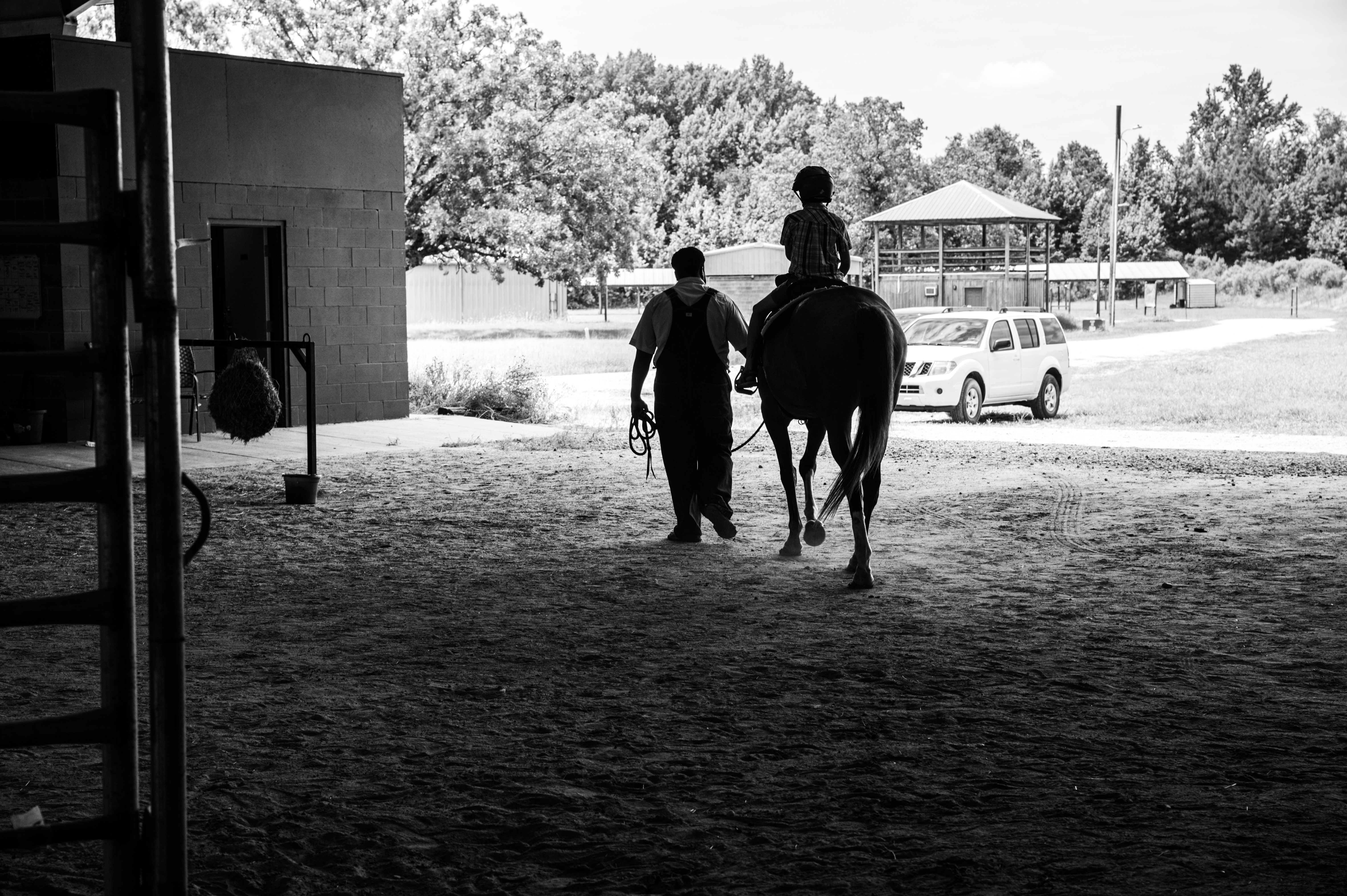 A boy riding a horse, accompanied by a man, riding away from the camera.