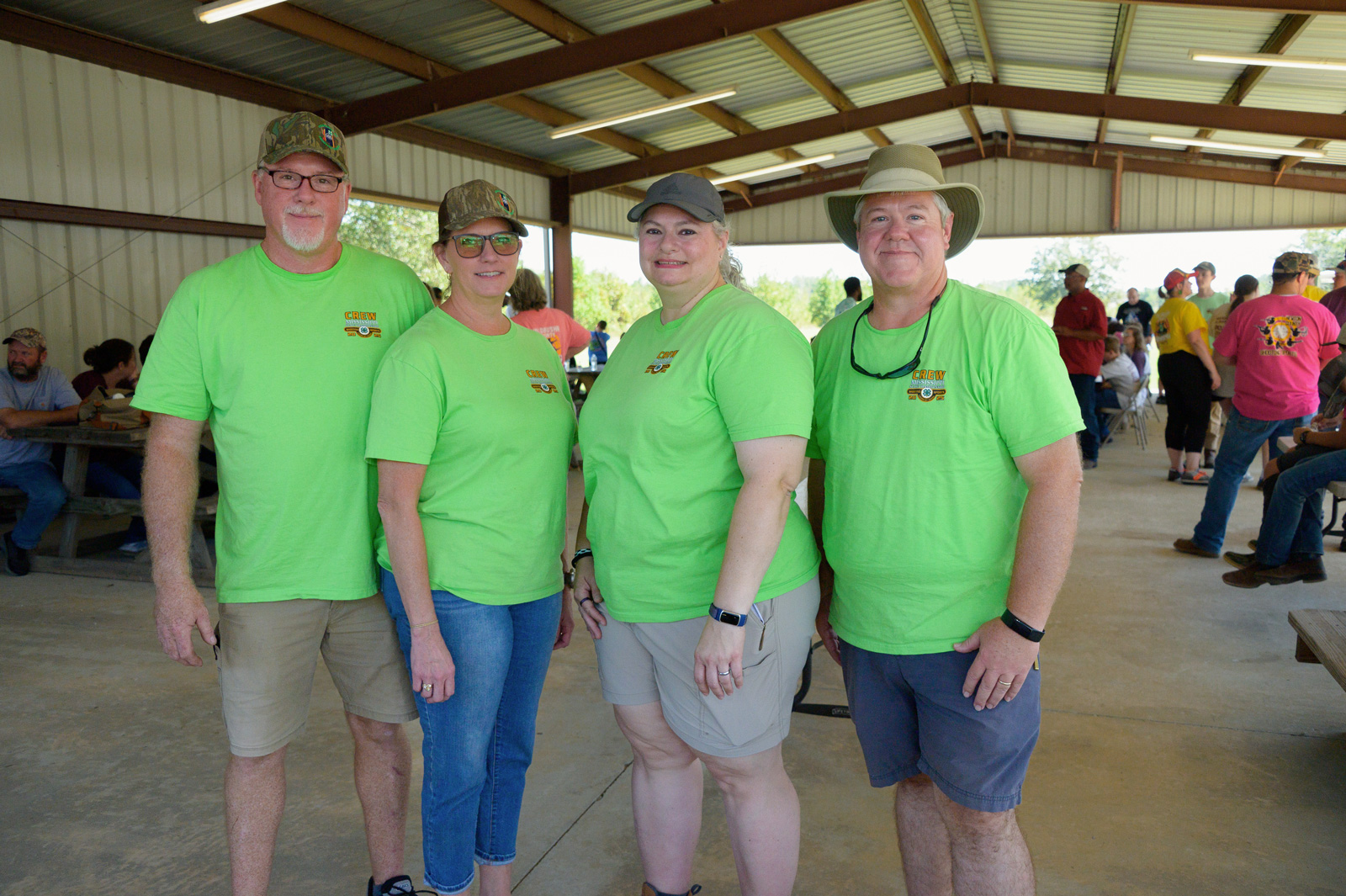 Four adults standing, smiling, and wearing green shirts.