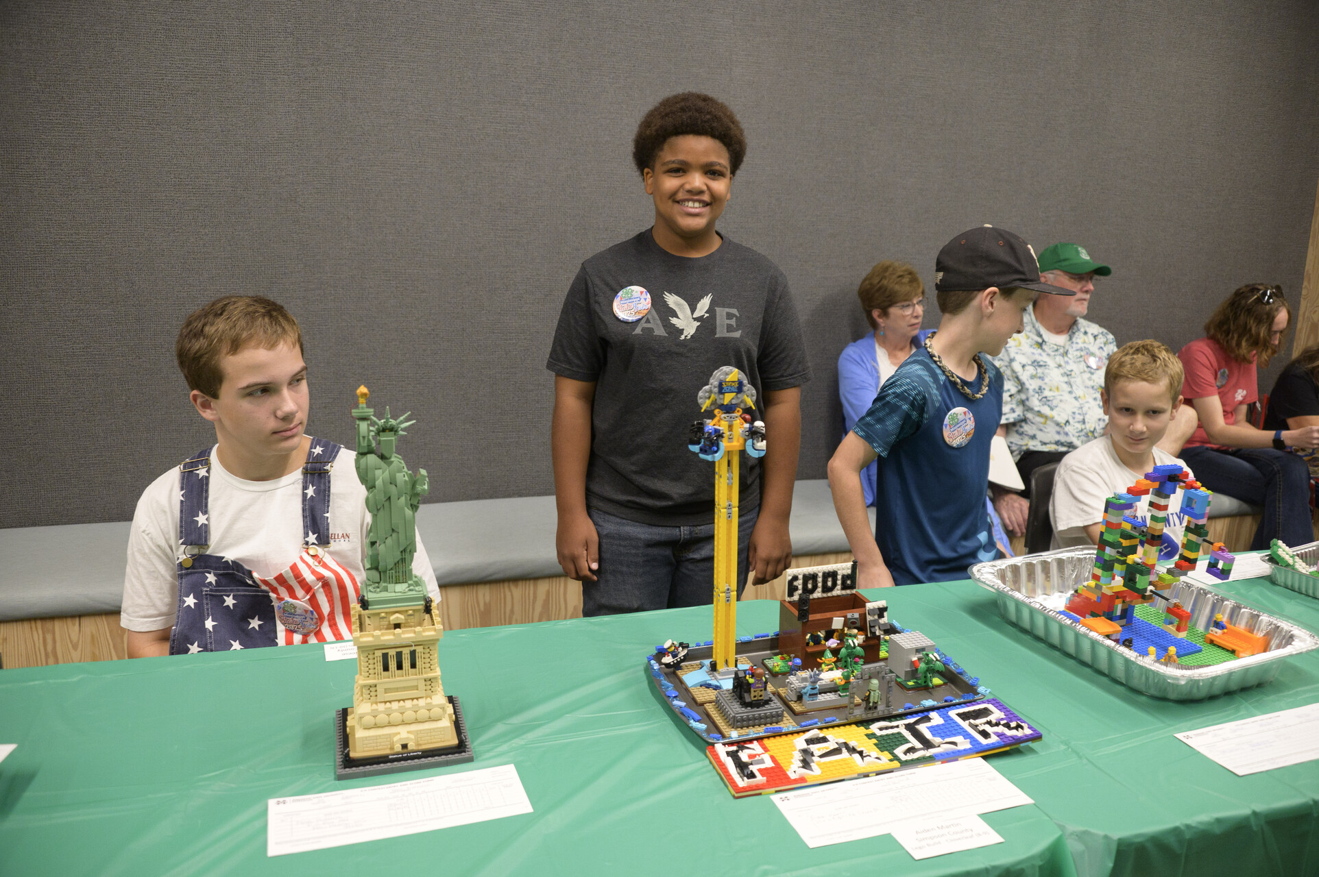 A group of young people, some standing and others seated, near LEGO builds.