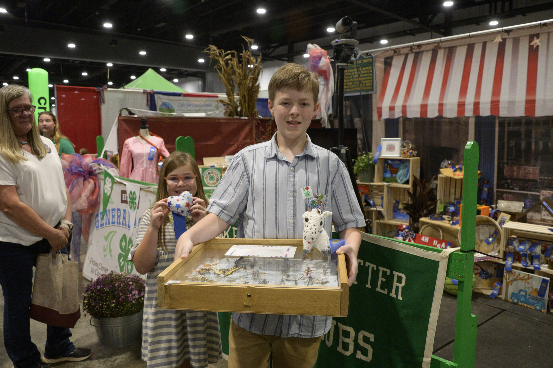 Two young people smiling, and one is holding an insect collection.