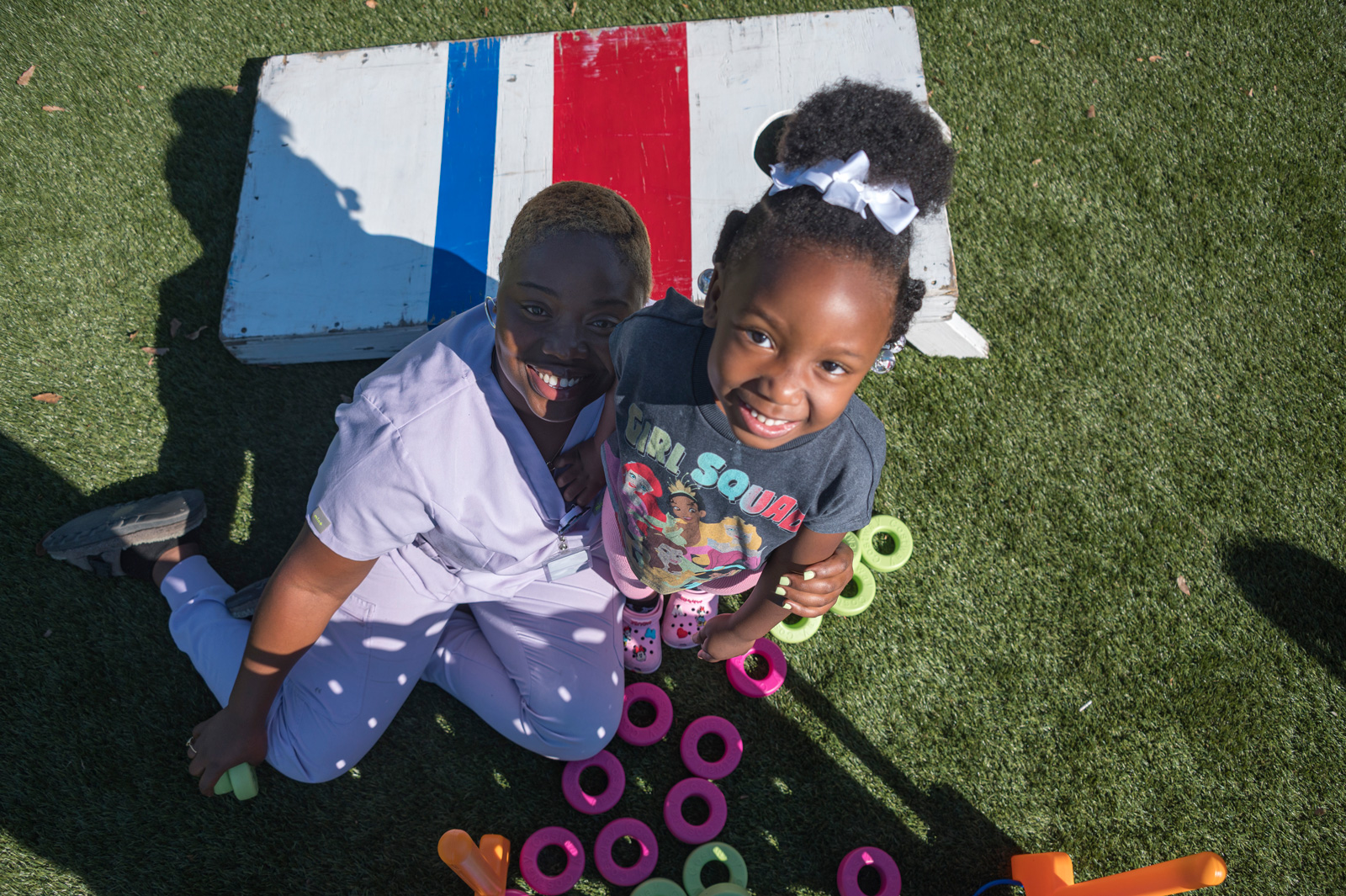 An adult and child, smiling up from an outdoor Connect 4 game.