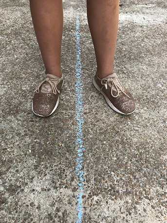 Two feet positioned on opposite sides of a blue chalk line on pavement.