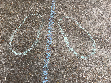 Two chalk outlines of feet positioned on opposite sides of a blue chalk line on pavement.