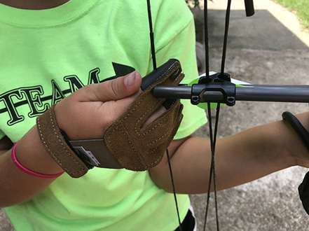 Close-up of a hand wearing a three-finger archery shooting glove, holding and pulling back the bowstring.
