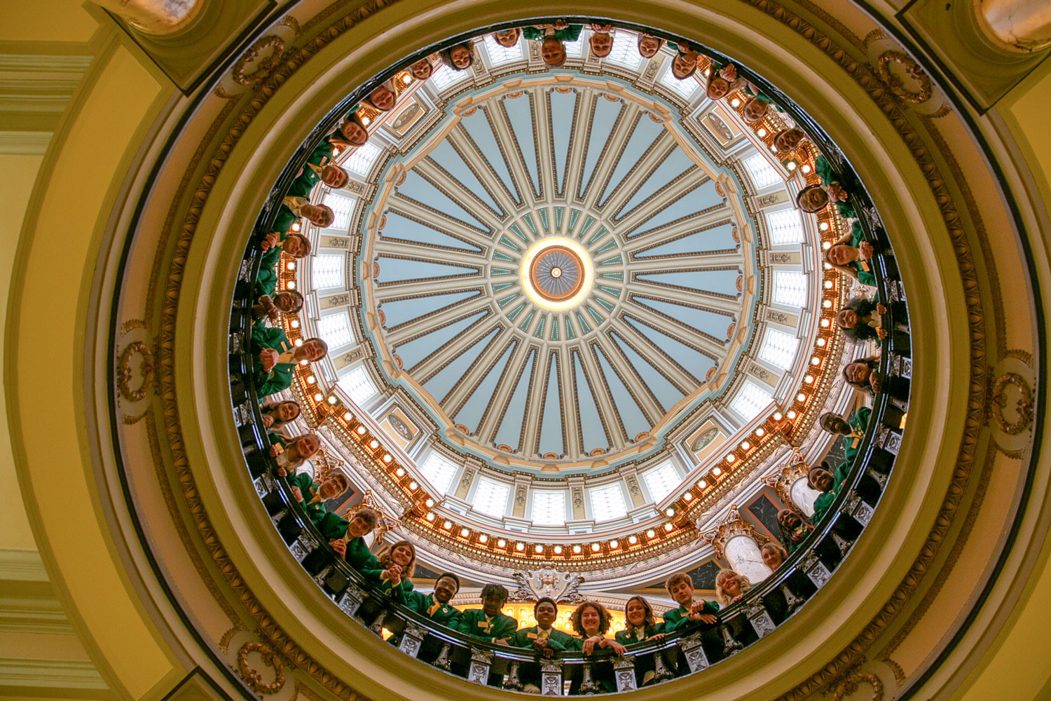 Young people wearing green jackets looking over a balcony in a rotunda.