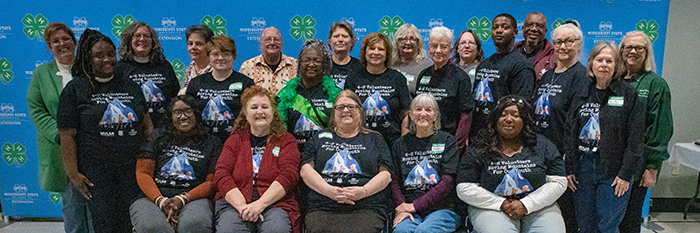 A group of MVLA officers stand and sit in front of a blue wall with MSU Extension and 4-H logos on it