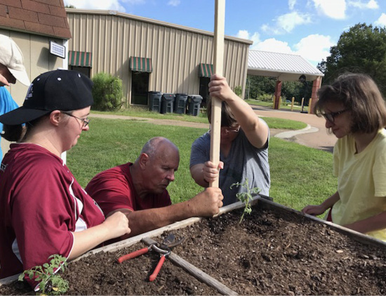Two people affix a pole to a raised gardening table while others watch.