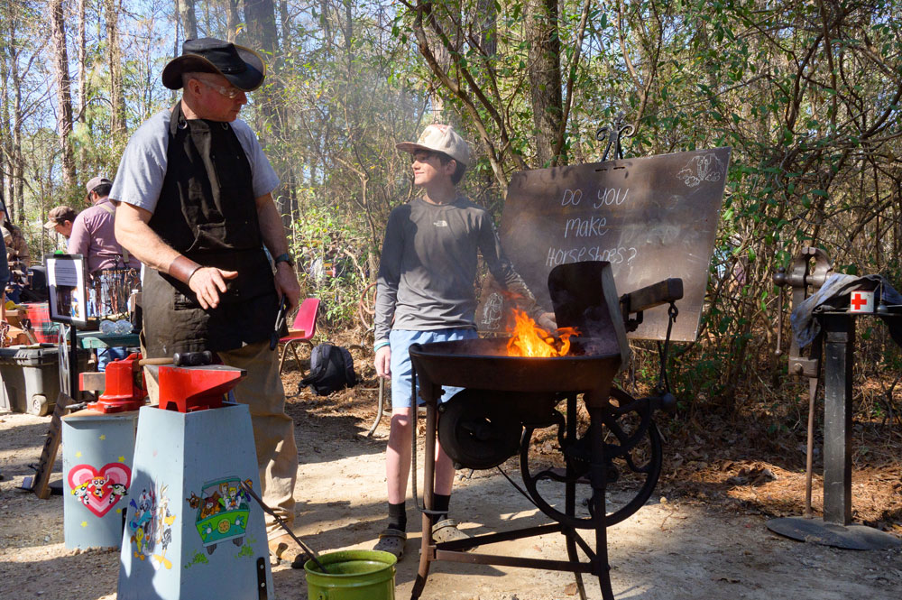 A person gestures near a forge fire as a child smiles.
