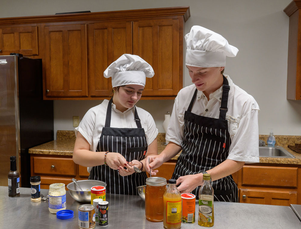 Two young people wearing chef's hats and mixing ingredients.