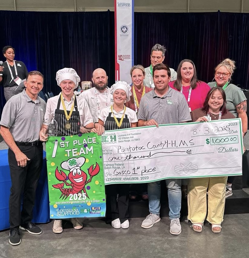 A group of people standing in front of a presentation banner and check, listing "1st place team" and "Pontotoc County 4-H: $1,000," respectively.