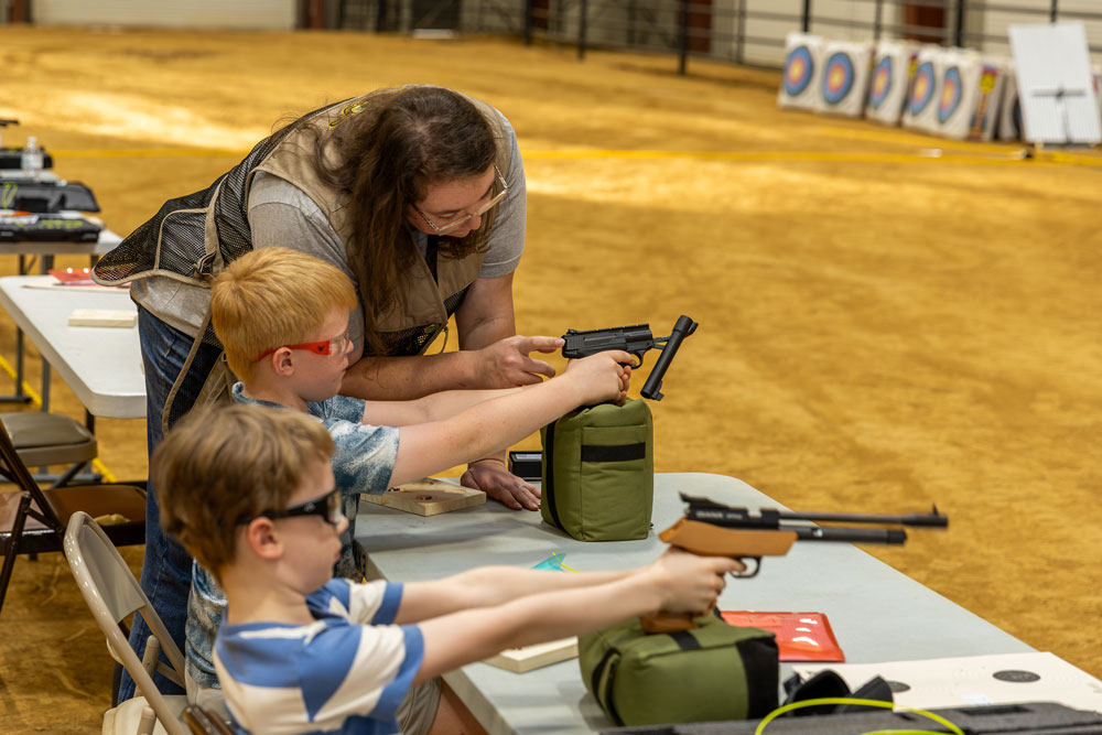 A person shows a child how to clear a pistol chamber.