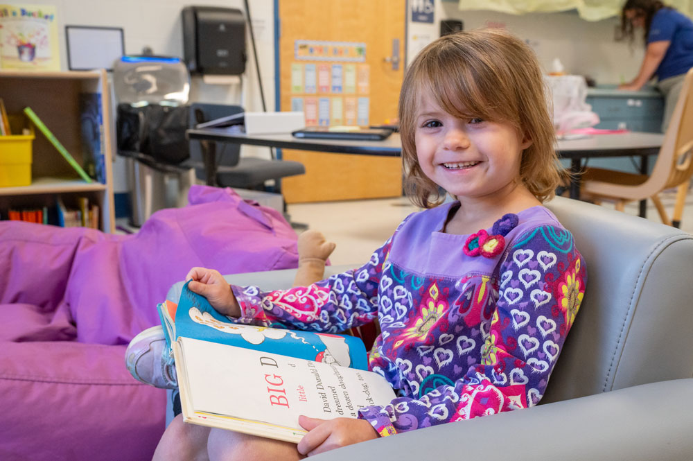 A child looking up from a book and smiling.